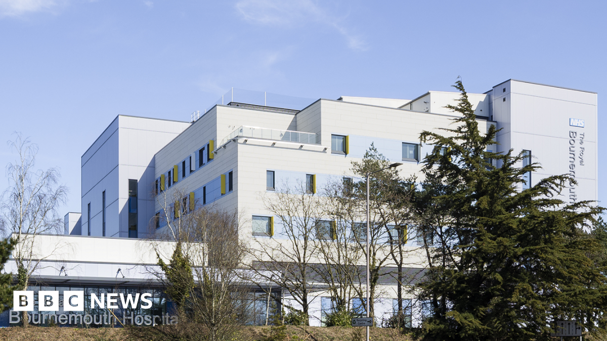 The Beach building at Royal Bournemouth Hospital, as seen from distance. The white, multi-storey, compartmented building sits on a grassy bank behind trees.