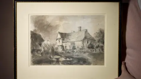 Roseberys The drawing of a house in the countryside within a black frame. A person wearing a pink top, whose face cannot be seen, holds the frame.