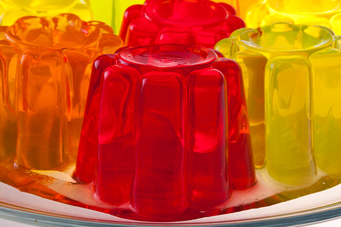 Colorful red, yellow, and orange gelatin desserts stacked closely in a clear dish, showing a glossy smooth texture.