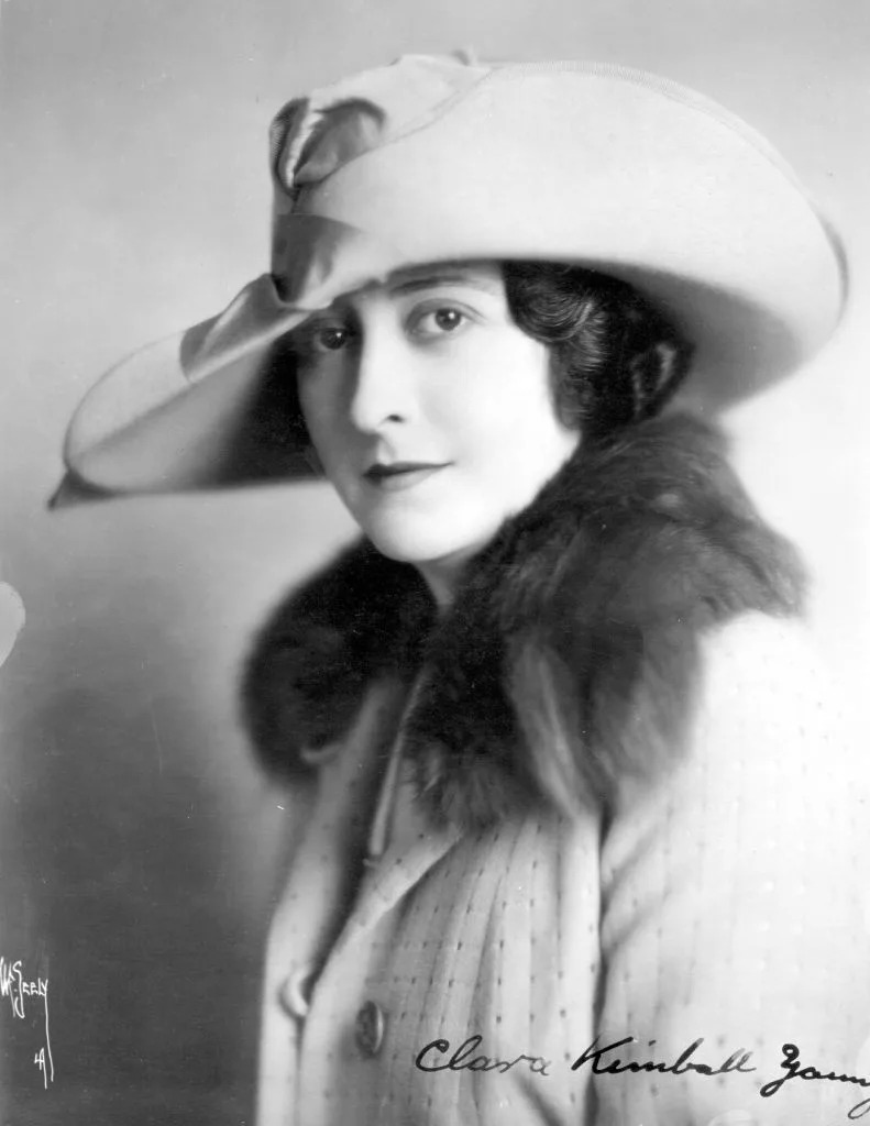 Young in vintage attire with fur collar and wide-brimmed hat from early 20th century, posing in a classic portrait