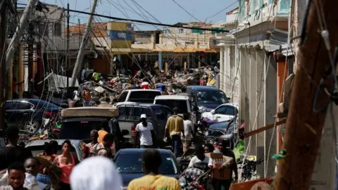 Reuters A crowded street filled with people and vehicles navigating wreckage - collapsed power lines hang low over the road and debris from damaged buildings is scattered everywhere
