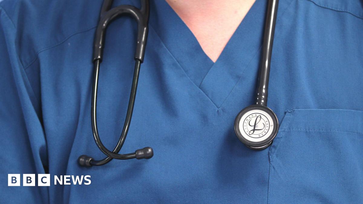 A medical person wears blue scrubs. A stethoscope hangs around their neck