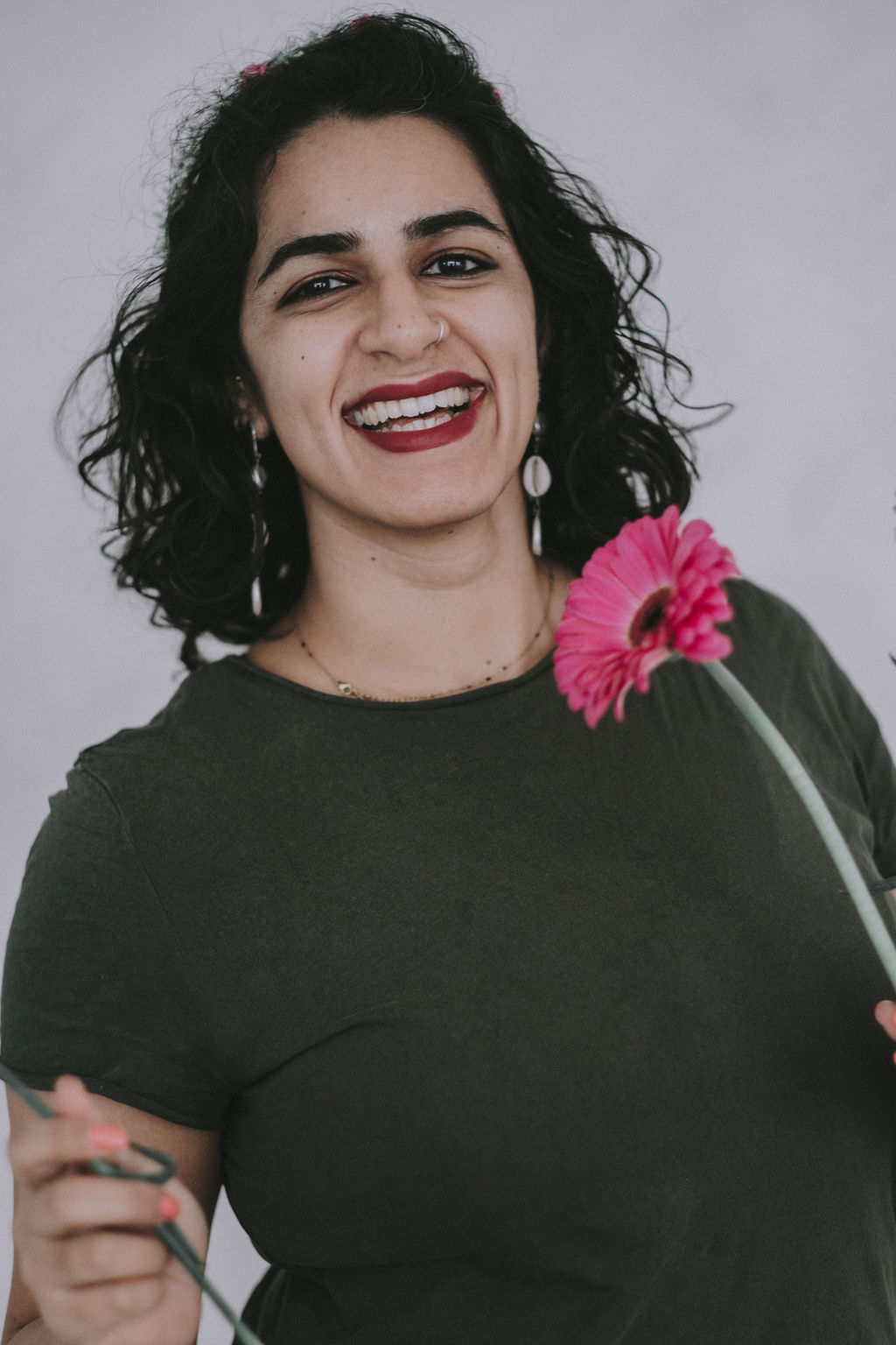 Maysun Hassanaly stands smiling at the camera holding a pink flower.