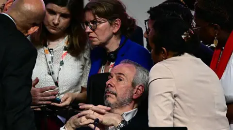 getty A bearded man, COP president Andre Correa do Lago lies back as several others surround him, looking worried, during  a critical moment in the COP30 talks