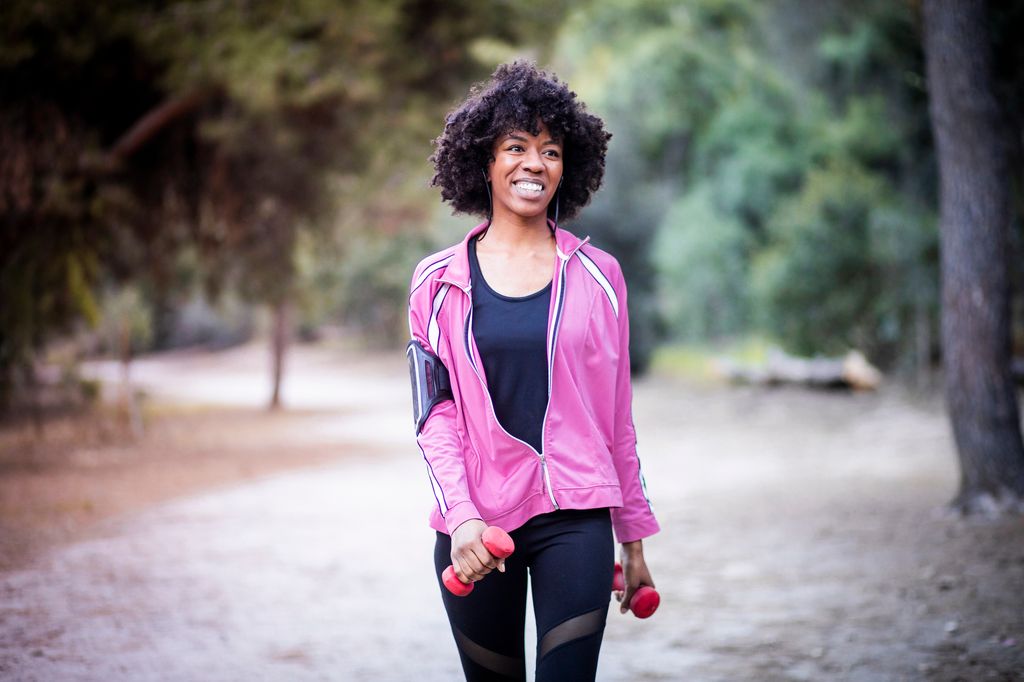 A young black woman walking and smiling with weights