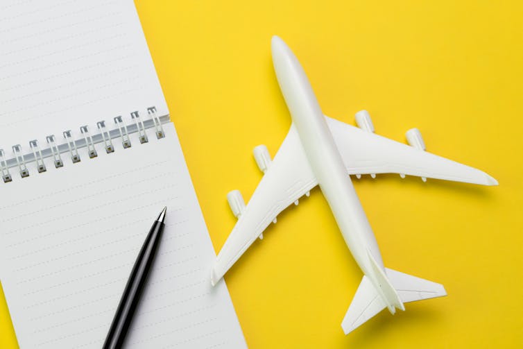 yellow background, white toy plane and white notebook with pen