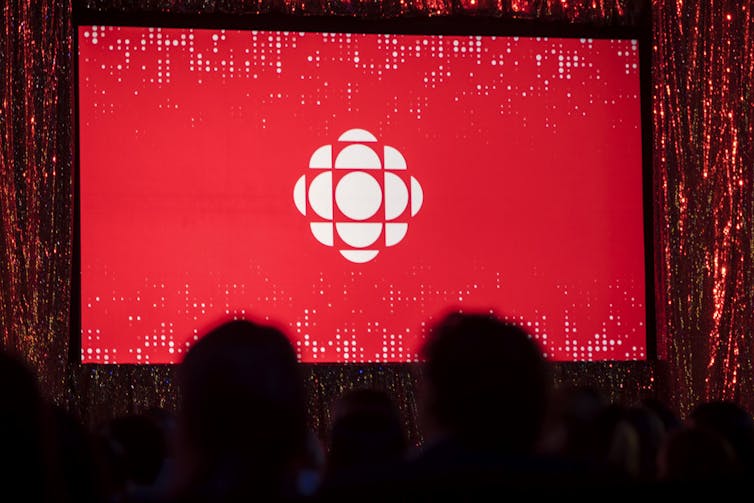 A crowd of people stand in front of a screen with the CBC logo projected onto it