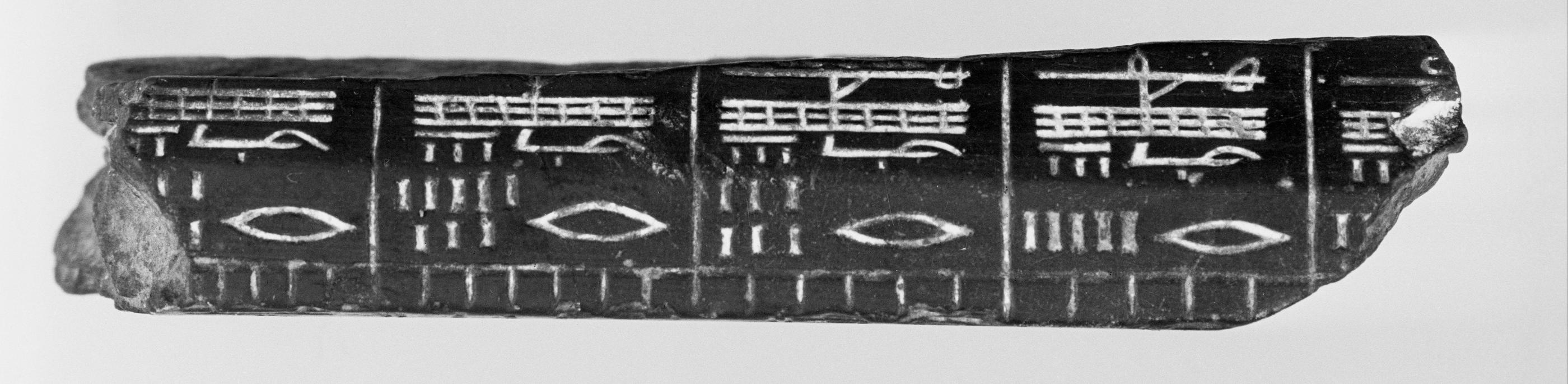 Ancient clay tablet fragment, approximately one meter long, featuring cuneiform script and numeric symbols arranged in rows and columns.