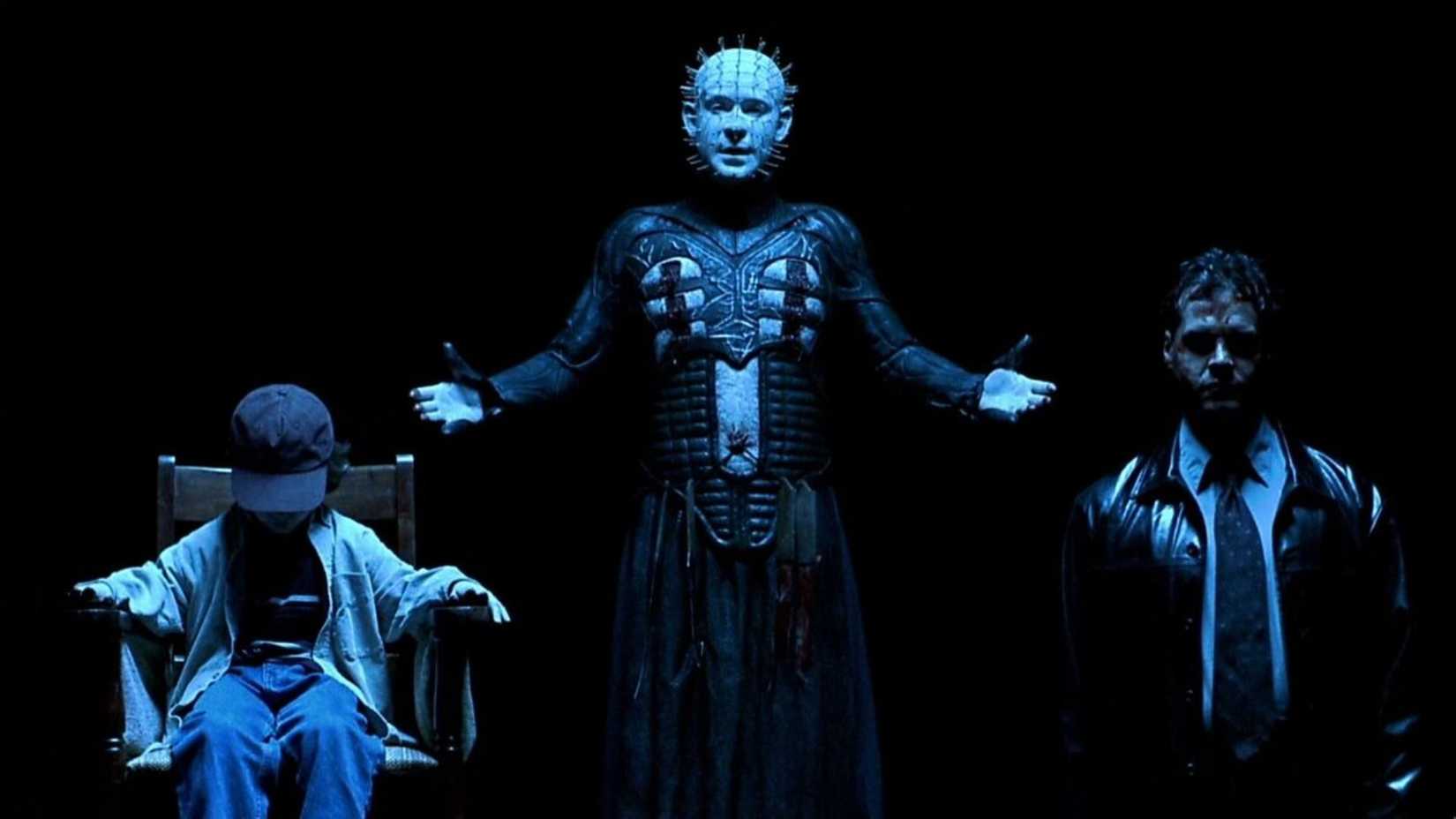 Pinhead stands beside a child and a man in a dark void in Hellraiser Inferno