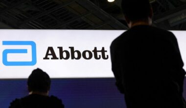 Two people stand in front of a large illuminated Abbott logo sign at a company booth.