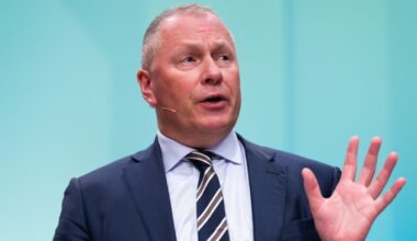 Nicolai Tangen speaks with one hand raised during a news conference, wearing a suit and striped tie.