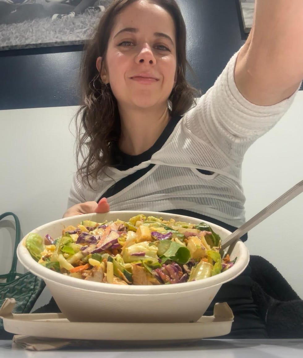 a bowl of salad on a table with a person holding a fork