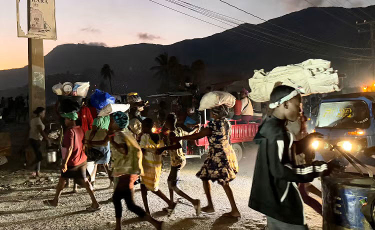 In Haiti, people carrying their belongings flee their homes  as night falls due to violence.