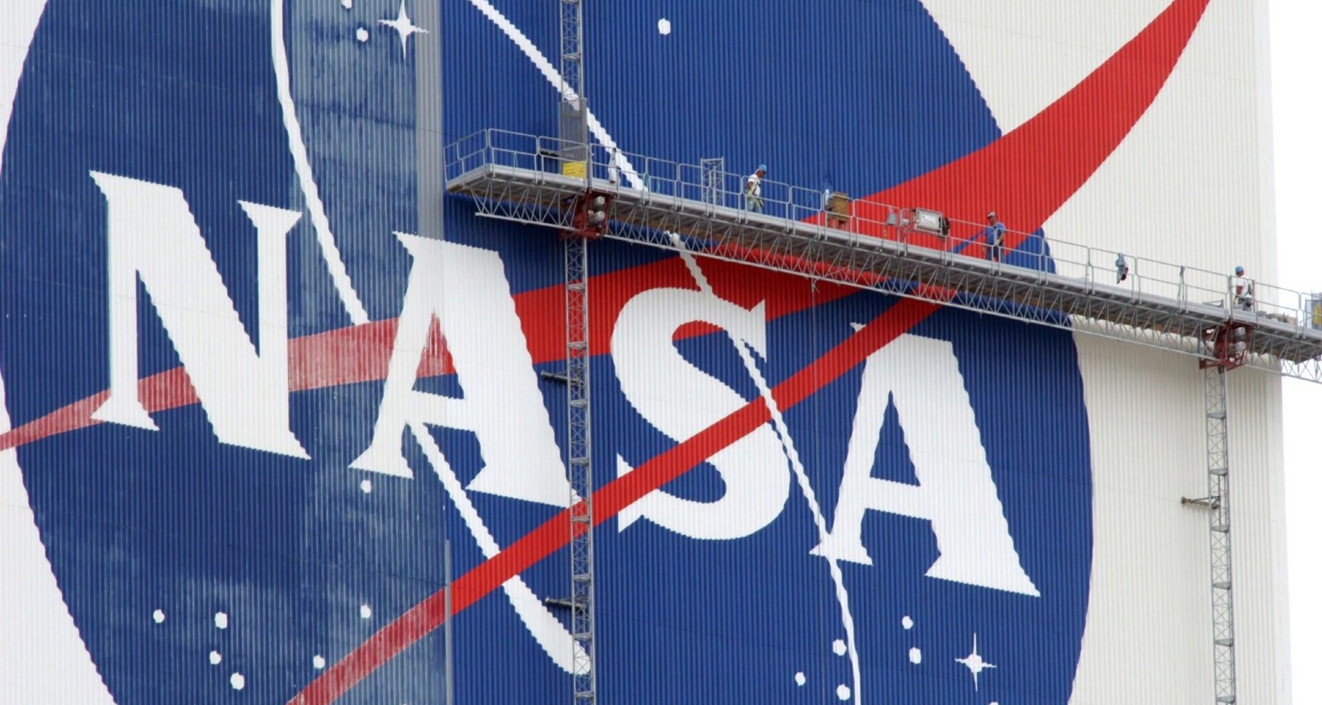 workers on scaffolding paint a nasa logo on a massive white building