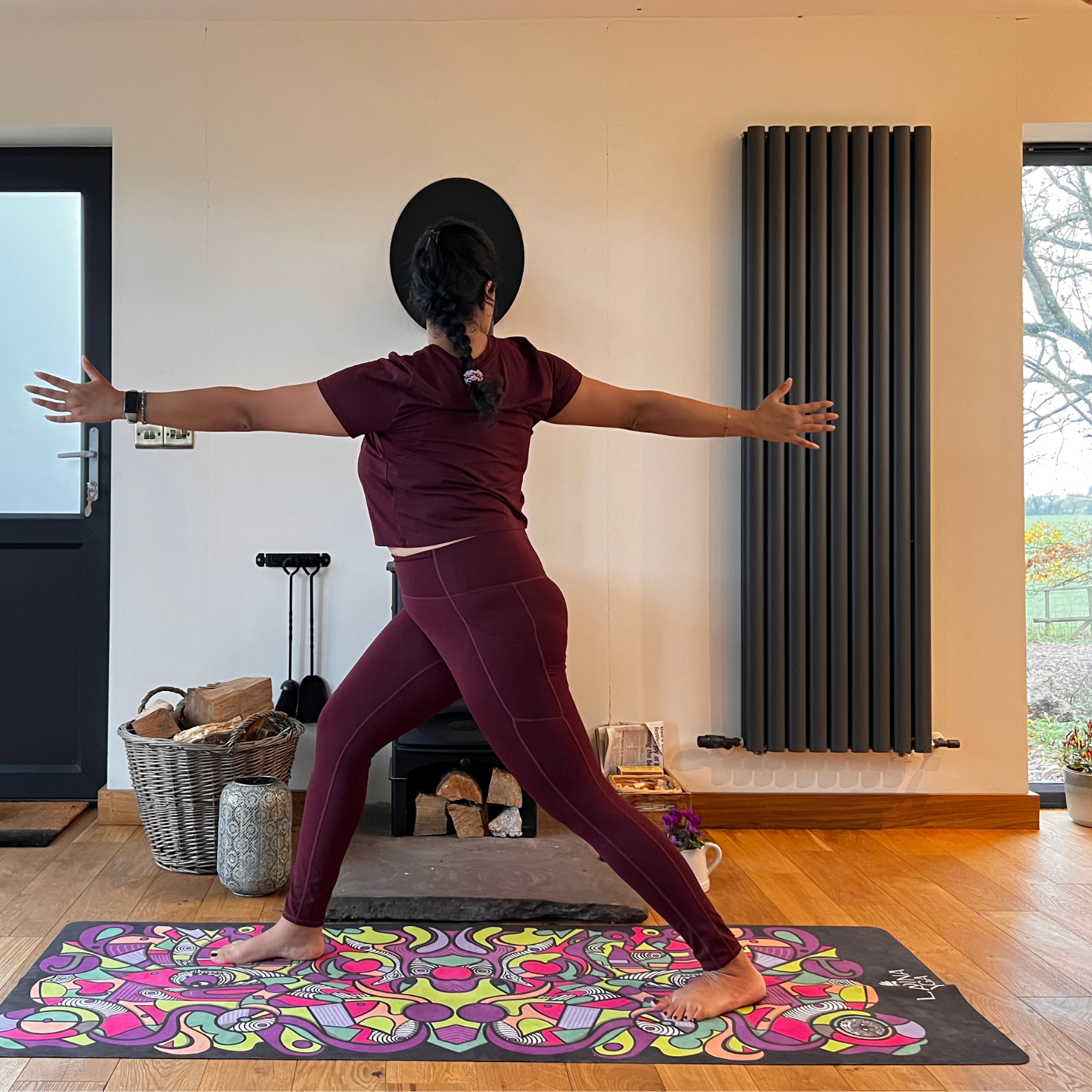 Maysun Hassanaly stands on a yoga mat performing revolved warrior. She is in a lunge position, with her right foot forward, right knee bent and left leg extended behind. Her torso is twisted to face right and her arms are extended at shoulder height.