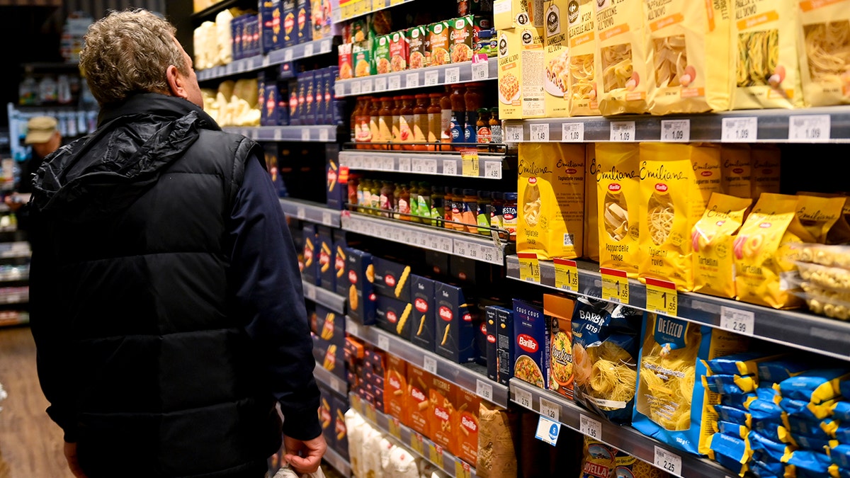 Man, seen from behind in black jacket, looks at different Italian pastas and egg noodles inside a supermarket on April 17, 2025 in Turin, Italy.