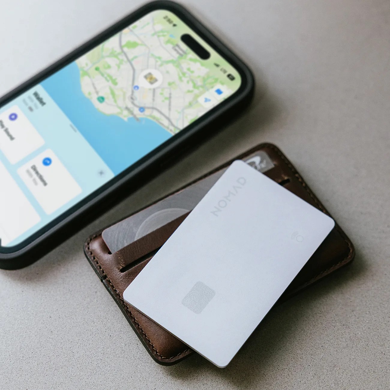 White OMAHON card partially inserted in a brown leather wallet next to a smartphone displaying a map.