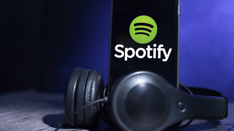 Smartphone displaying the Spotify logo placed beside a pair of headphones