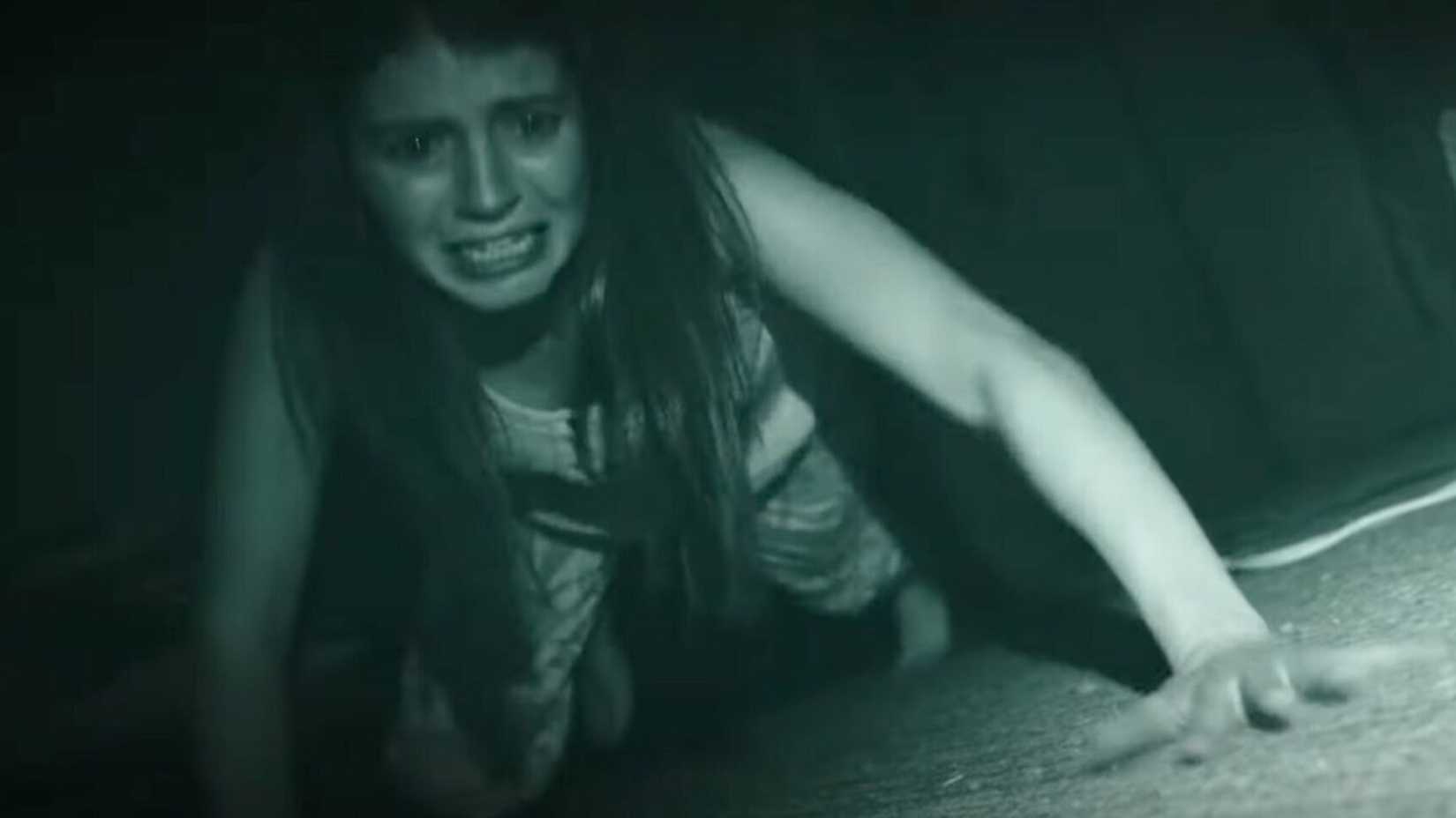 A woman crawls on the ground looking scared in Paranormal Activity Next of Kin