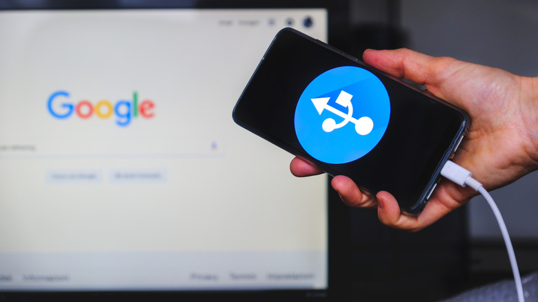 Smartphone with USB logo on screen connected to computer displaying Google page