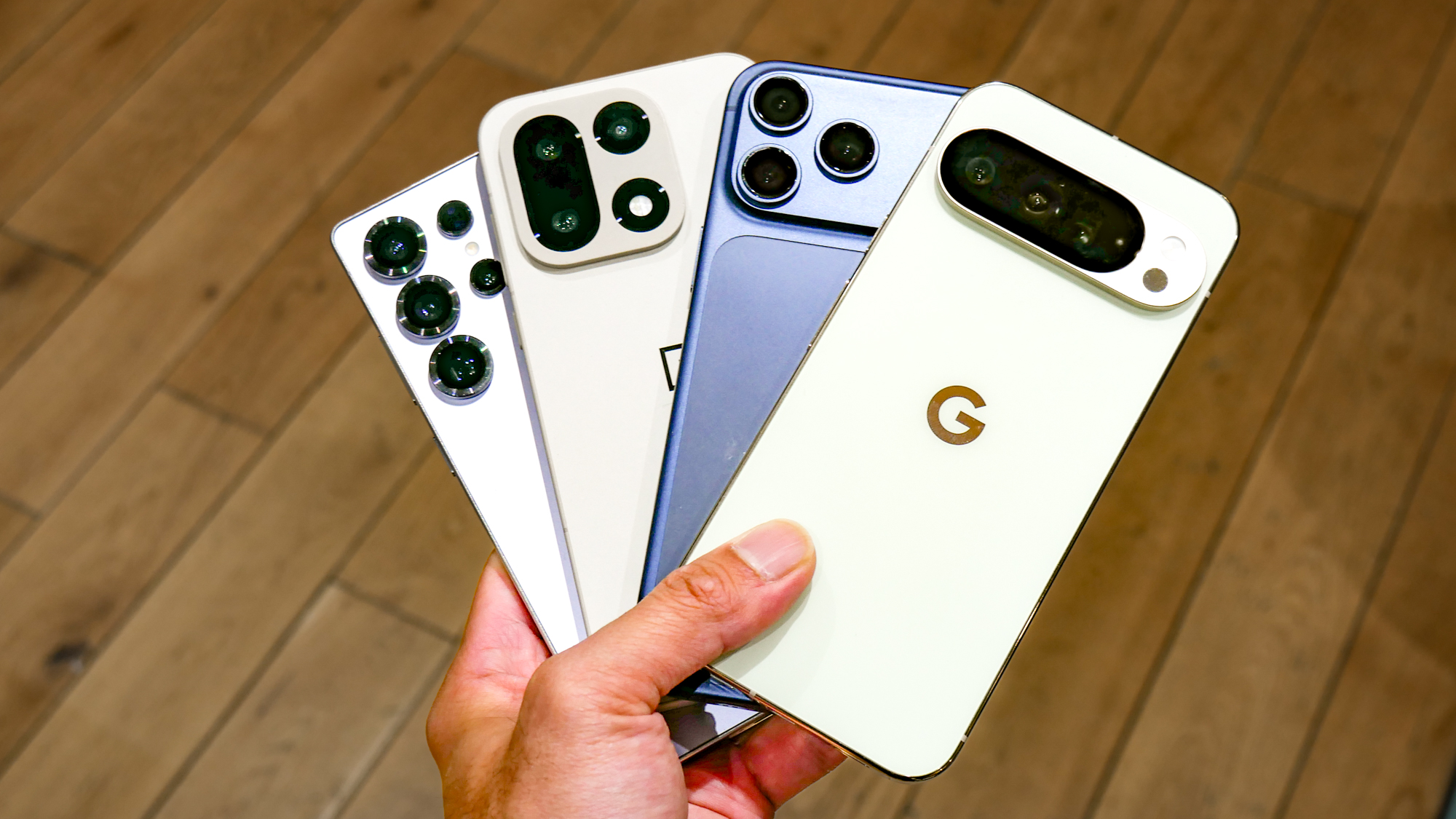 iPhone 17 Pro Max, Galaxy S25 Ultra, OnePlus 15, and Pixel 10 Pro XL held in the hand.