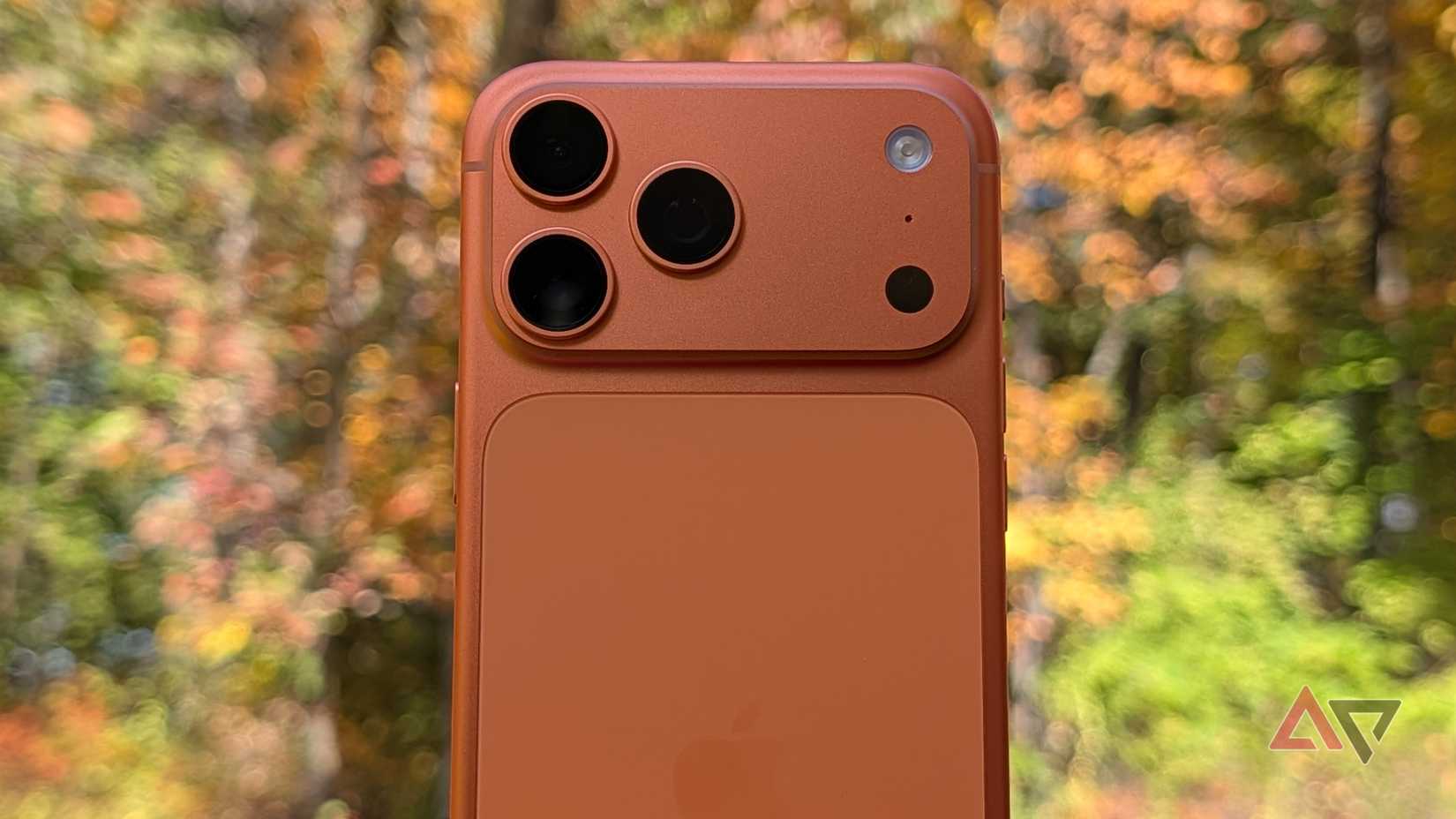 iPhone 17 Pro Max in Cosmic Orange held up against woods