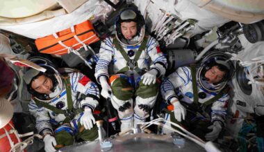 A photograph of three astronauts wearing white space suits huddled in a spacecraft.