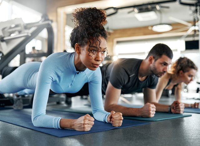 African american woman doing plank on exercise mat with two other people during group workout in gym. Concept: fitness training.