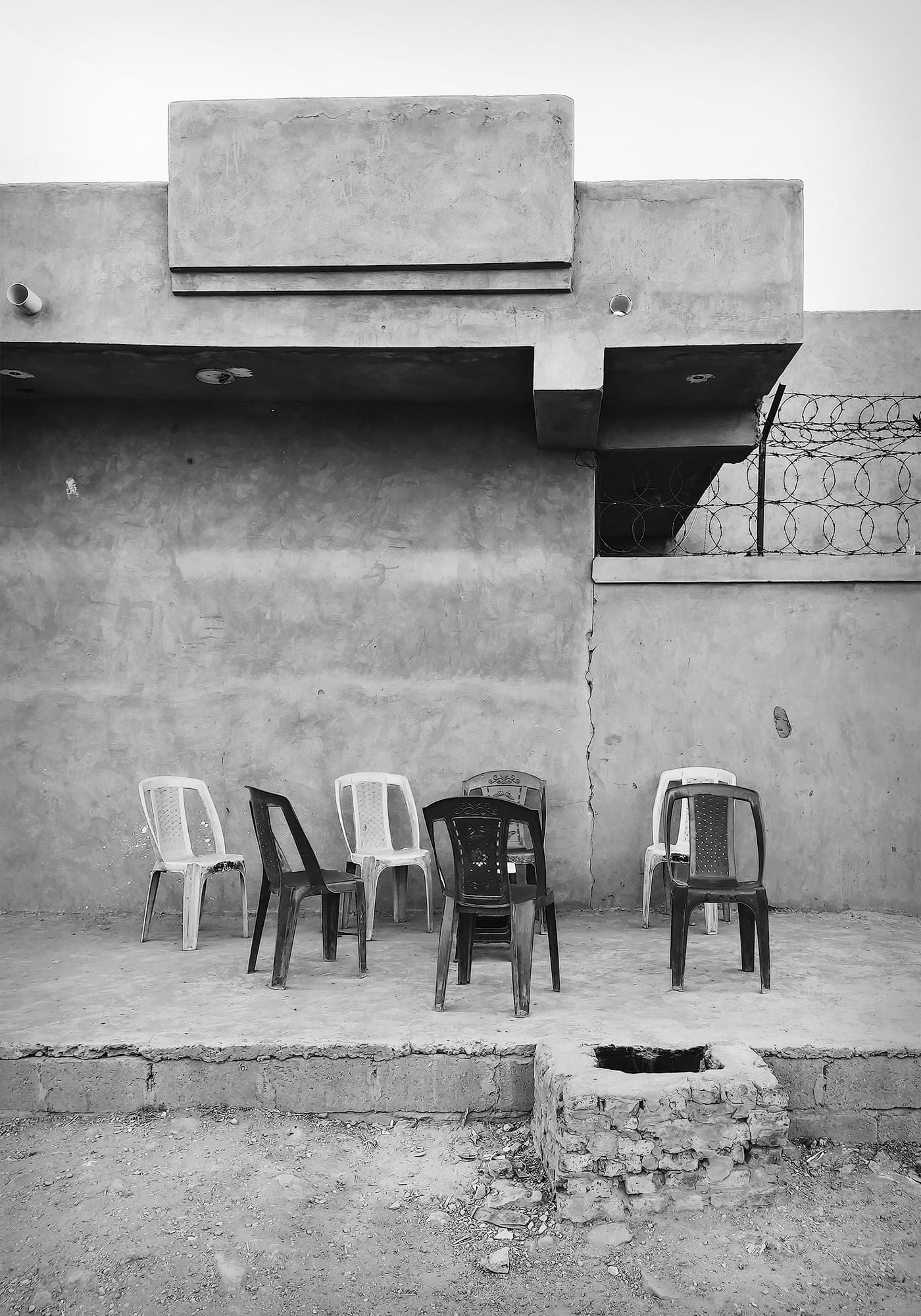 a black-and-white photo by Mohamed Abuagla of plastic chairs arranged in a circle on a sidewalk, but no people around