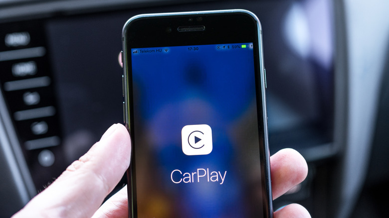 A person holding an iPhone that shows the CarPlay logo.