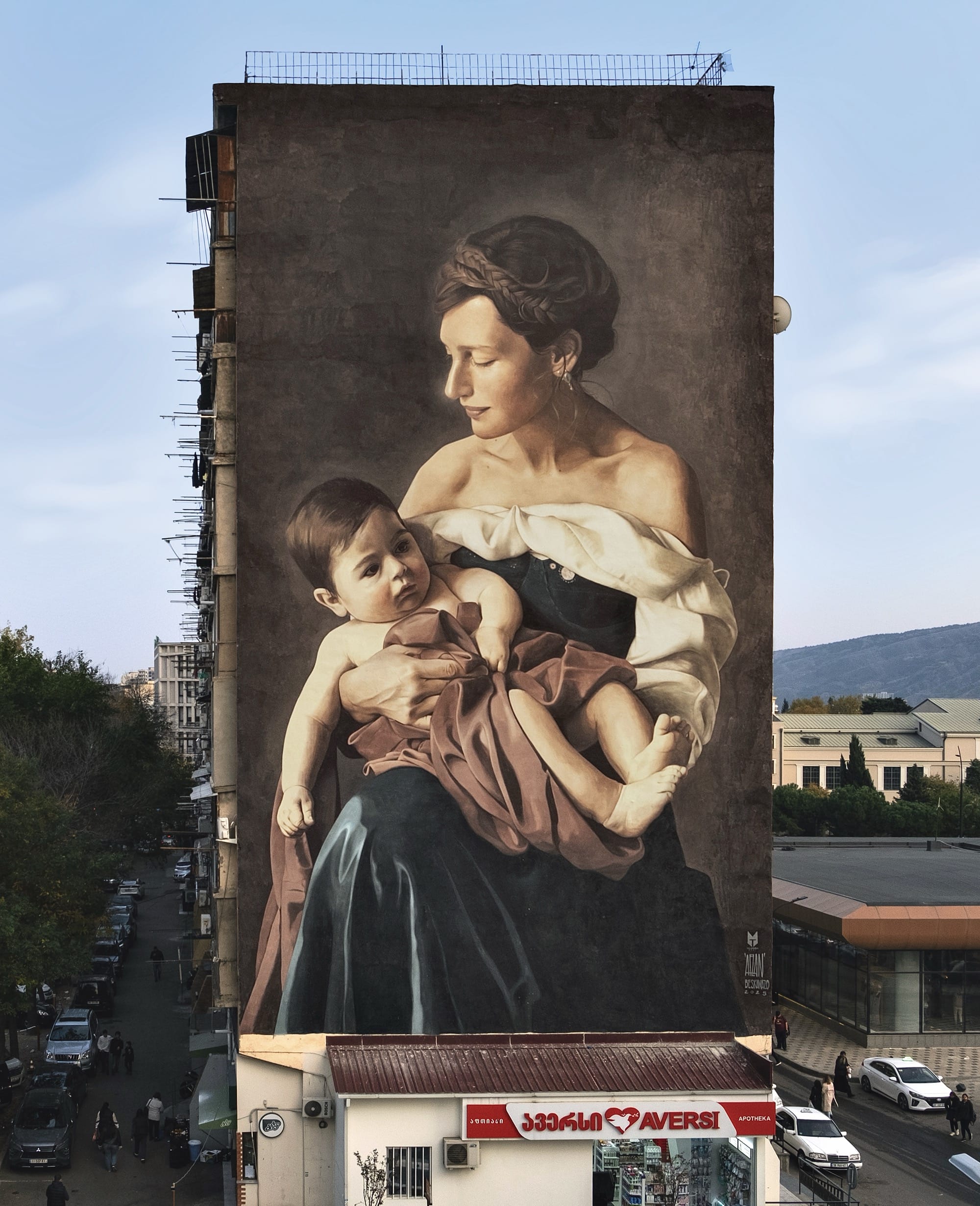 a mural on the side of a tall building featuring a mother holding her baby in her arms