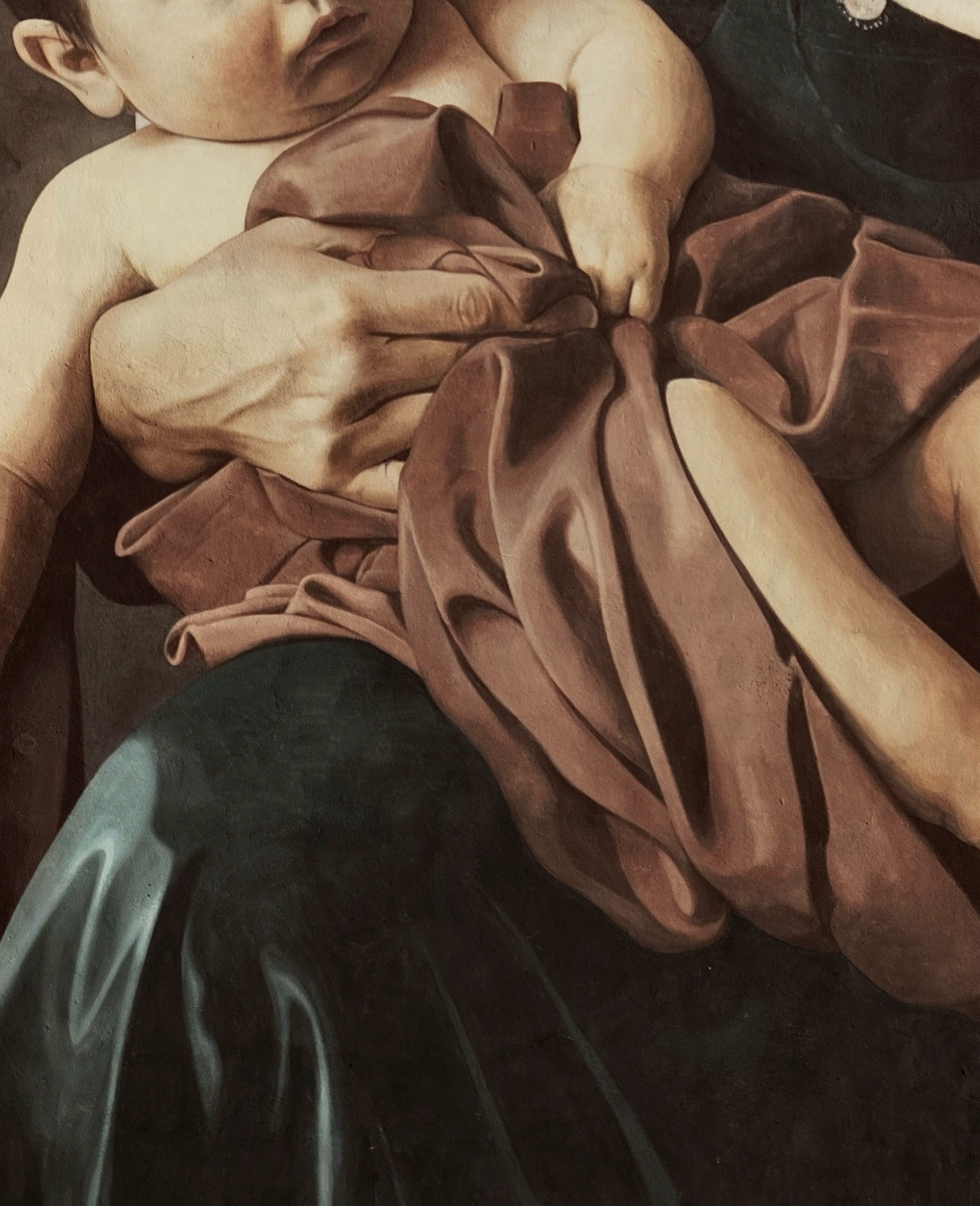 a detail of a a mural on the side of a tall building featuring a mother holding her baby in her arms