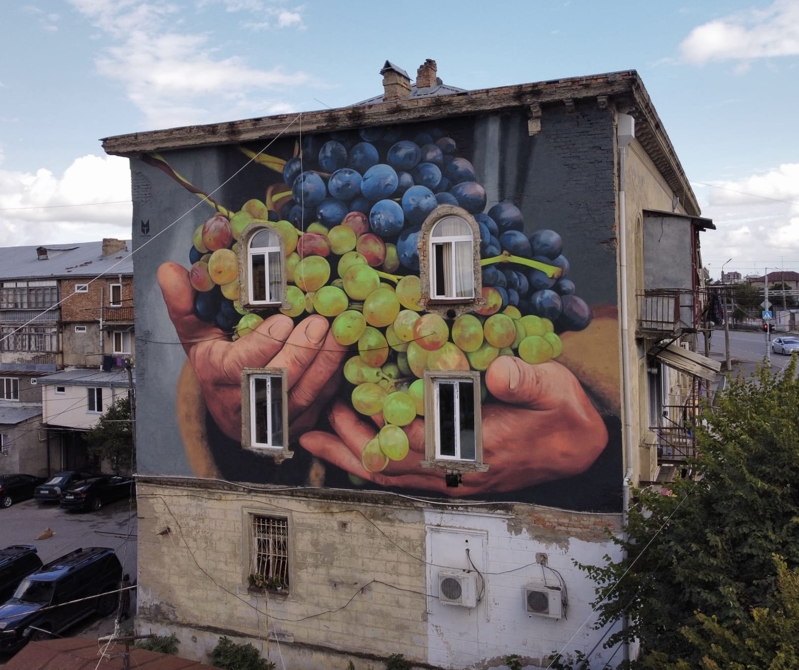 a mural on the side of a building of two hands holding a pile of grapes
