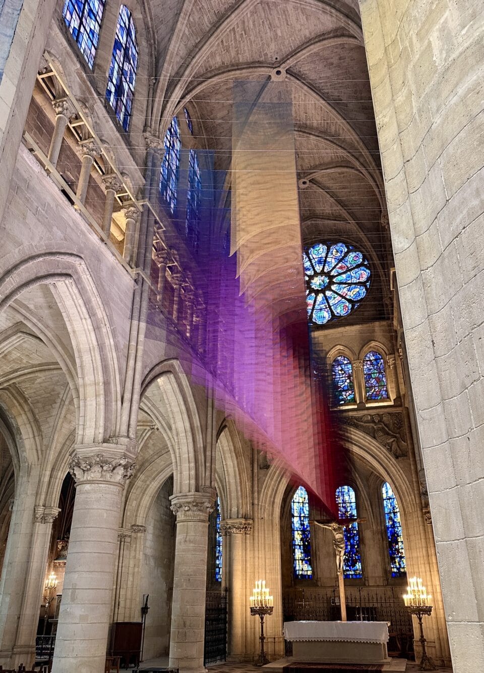 an art installation by Tomislav Topić of layers of colorful planes of fabric suspended inside of a cathedral, making a gradient of pink, blue, and yellow
