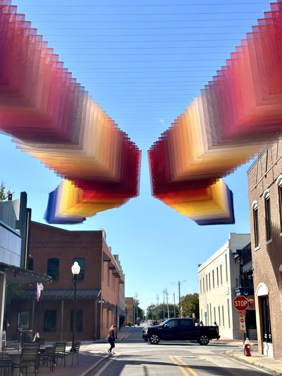 an art installation by Tomislav Topić of layers of colorful planes of fabric suspended above a street, between two buildings, in undulating rows so that it looks prismatic