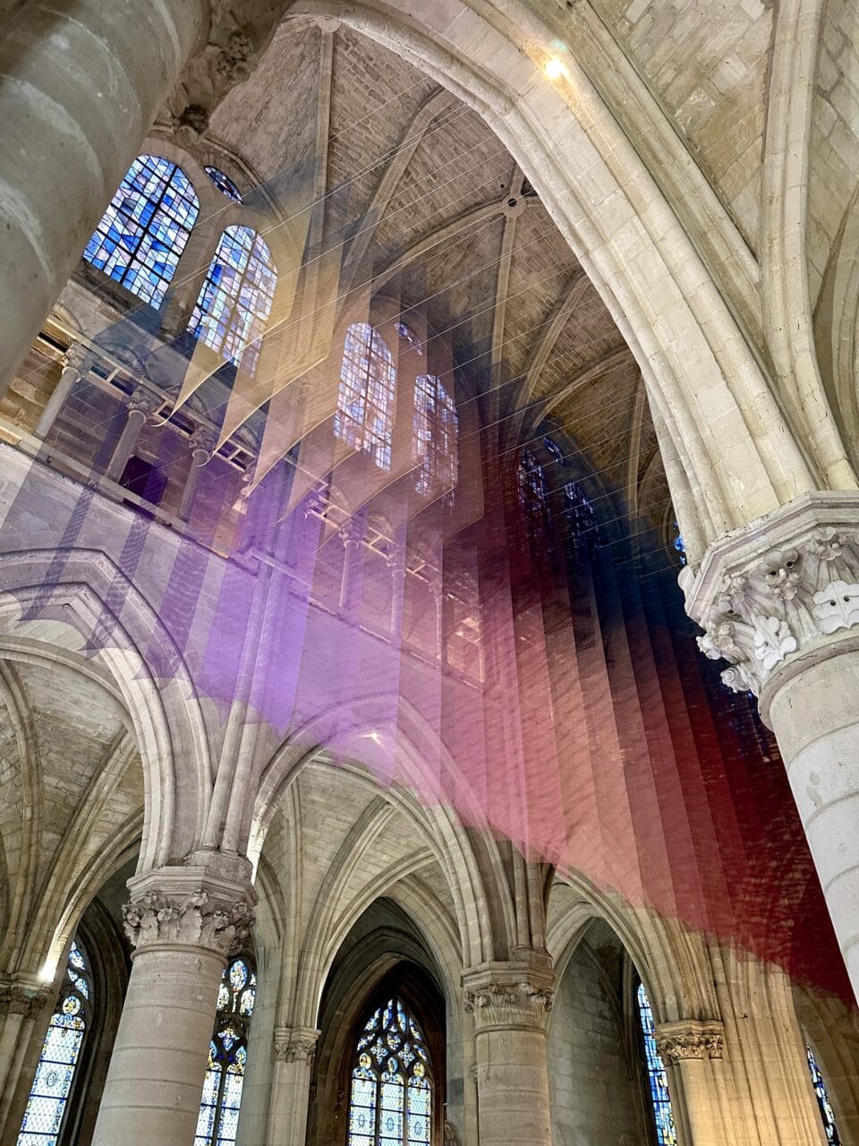 an art installation by Tomislav Topić of layers of colorful planes of fabric suspended inside of a cathedral, making a gradient of pink, blue, and yellow