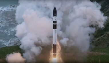 a black and white rocket launches from a seaside pad