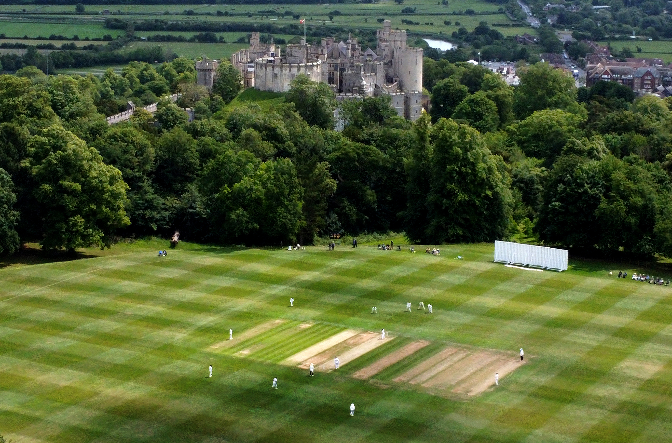 Cricket players on a green field with Arundel Castle in the background.