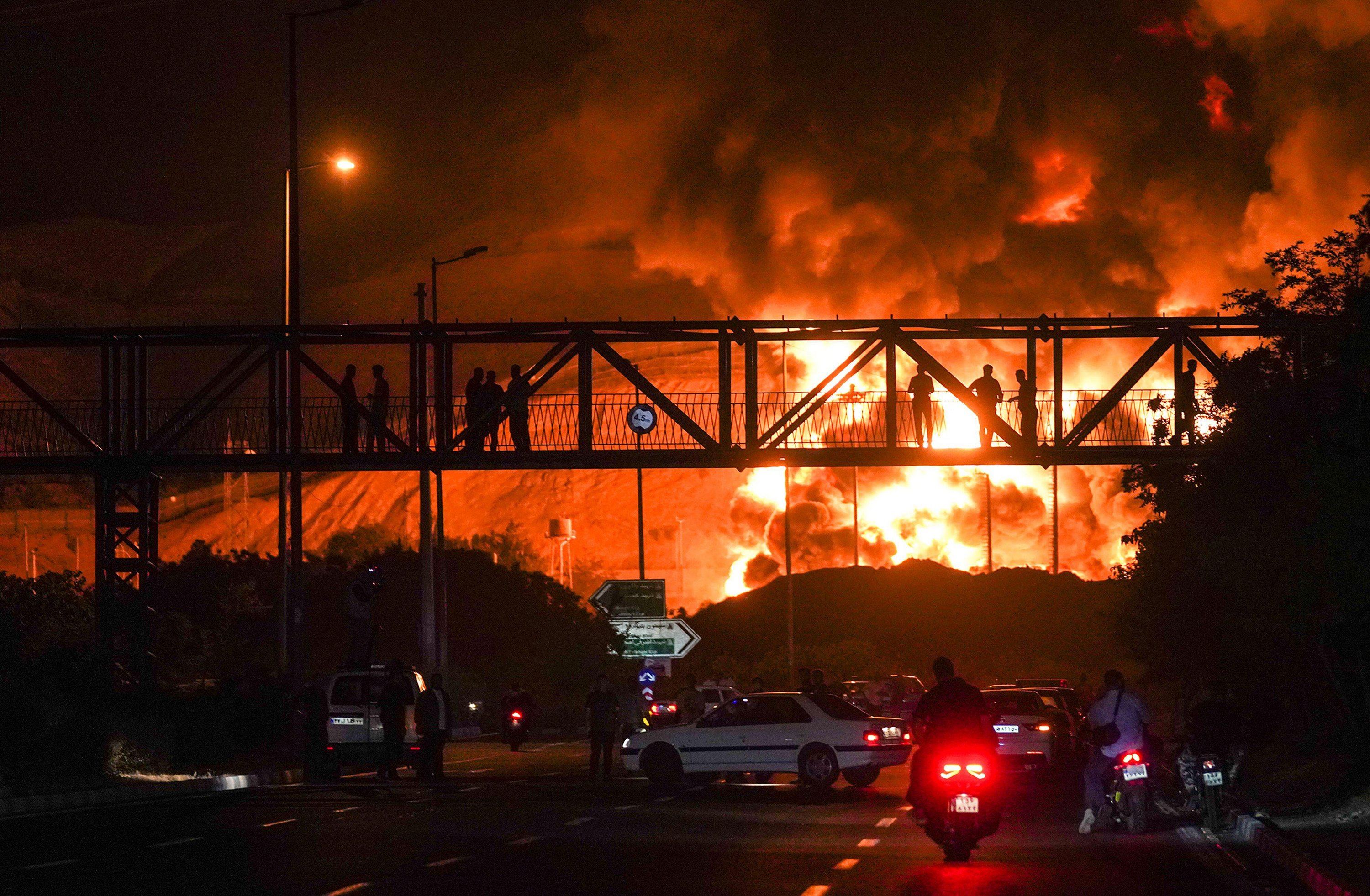 Iranians look on as a plume of smoke and fire rises from an oil refinery in Tehran after an overnight Israeli strike.