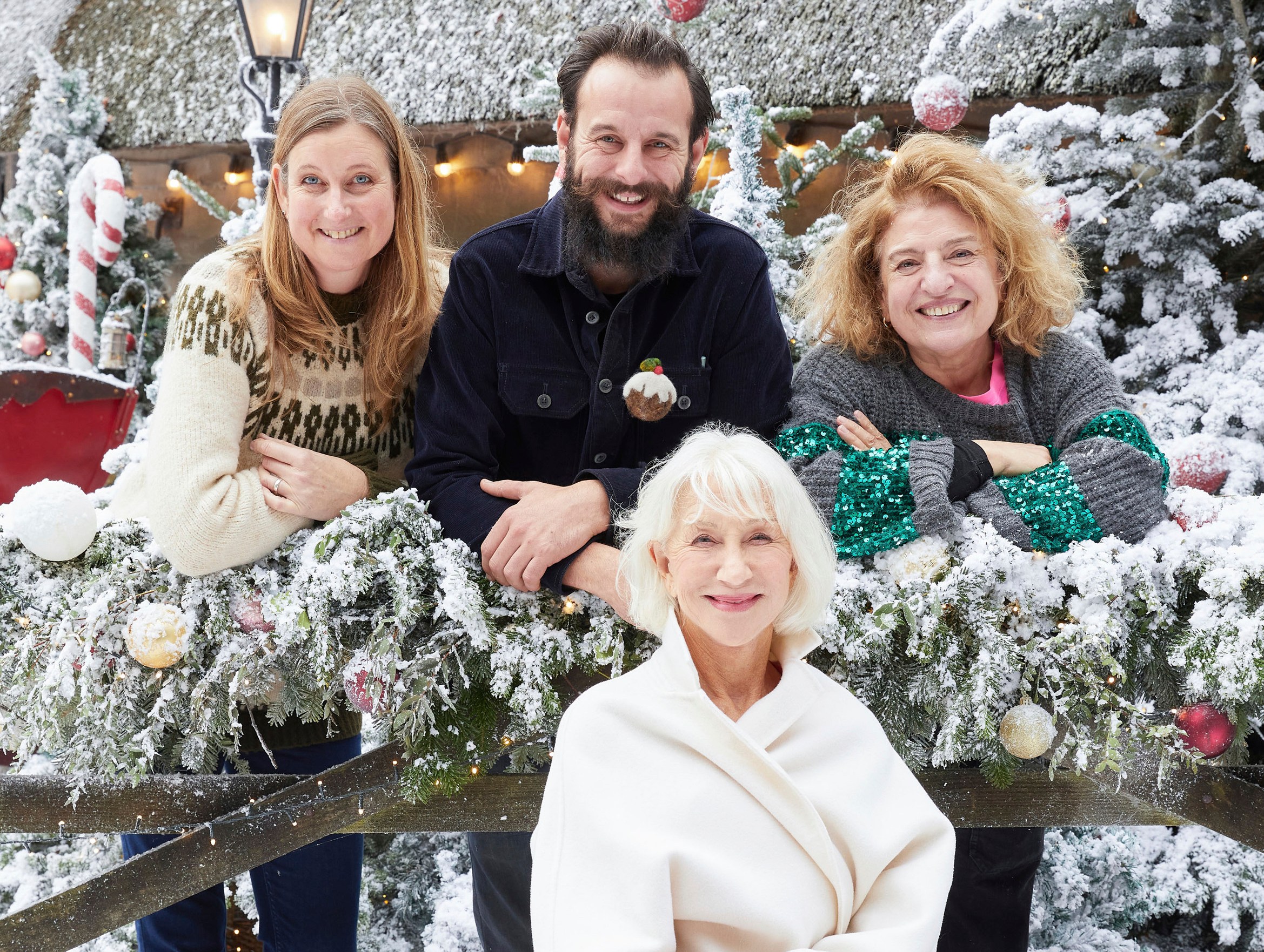 Four people and one seated woman smile in front of snow-covered Christmas decor.
