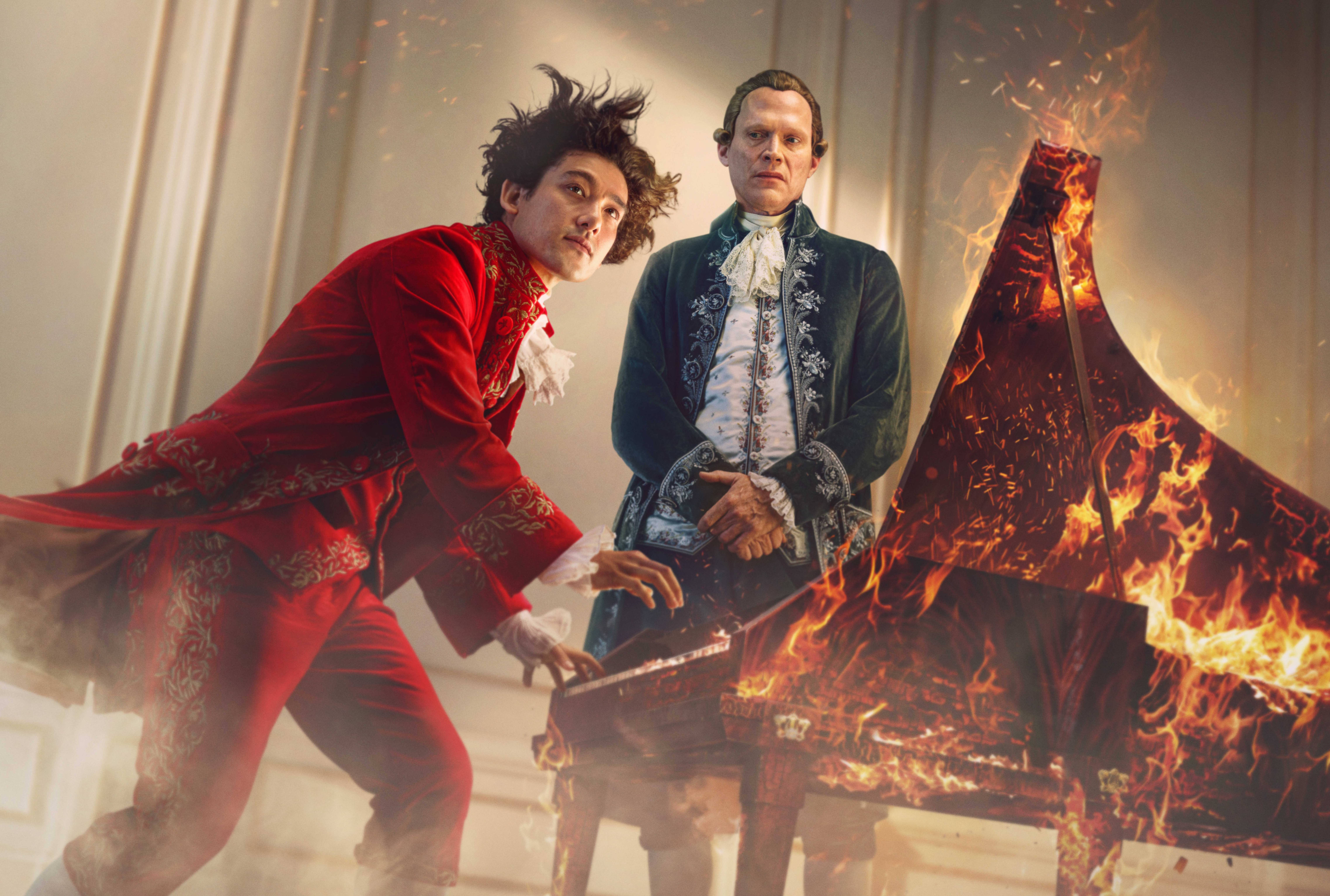 Amadeus key art, with two men in period clothing, one playing a flaming piano.