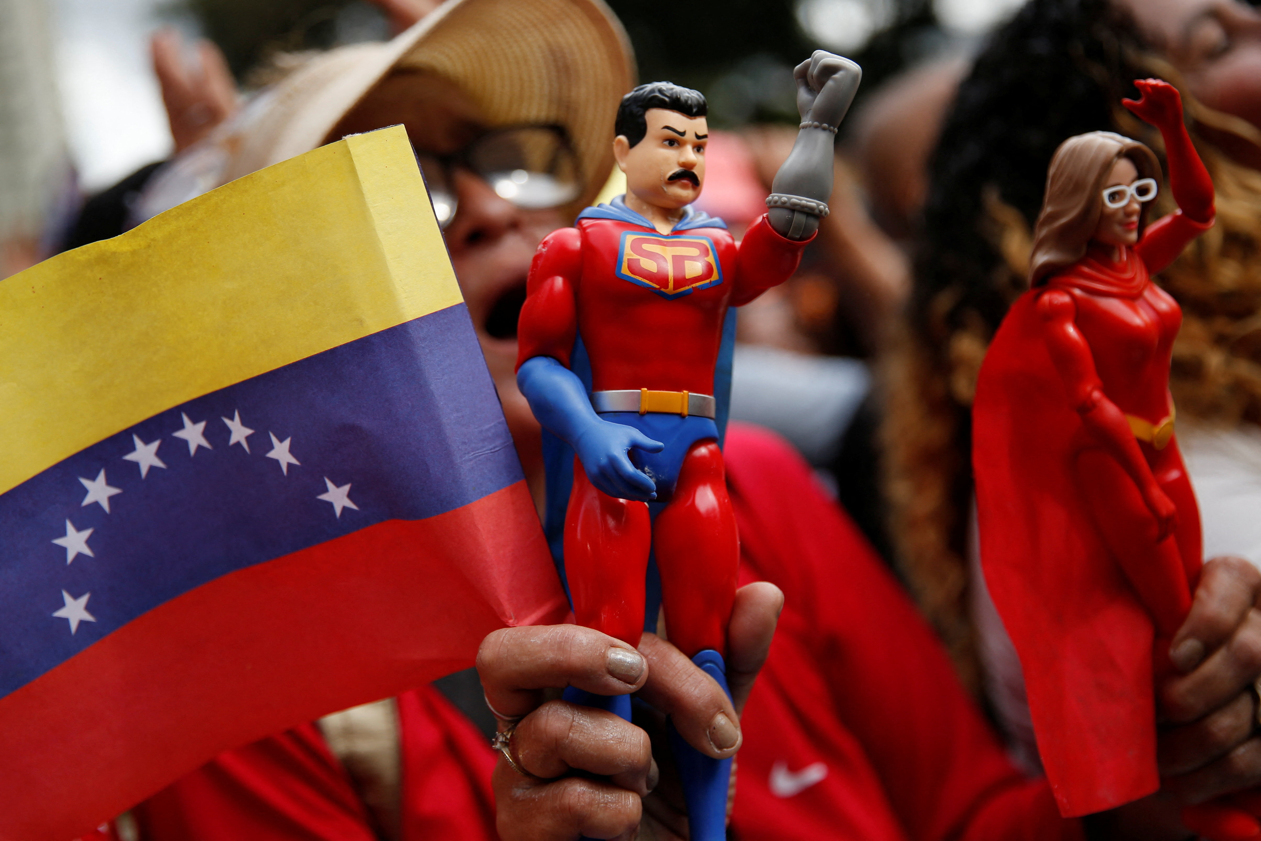 A supporter holds a "Super Bigote" action figure and a Venezuelan flag during a ceremony in Caracas.