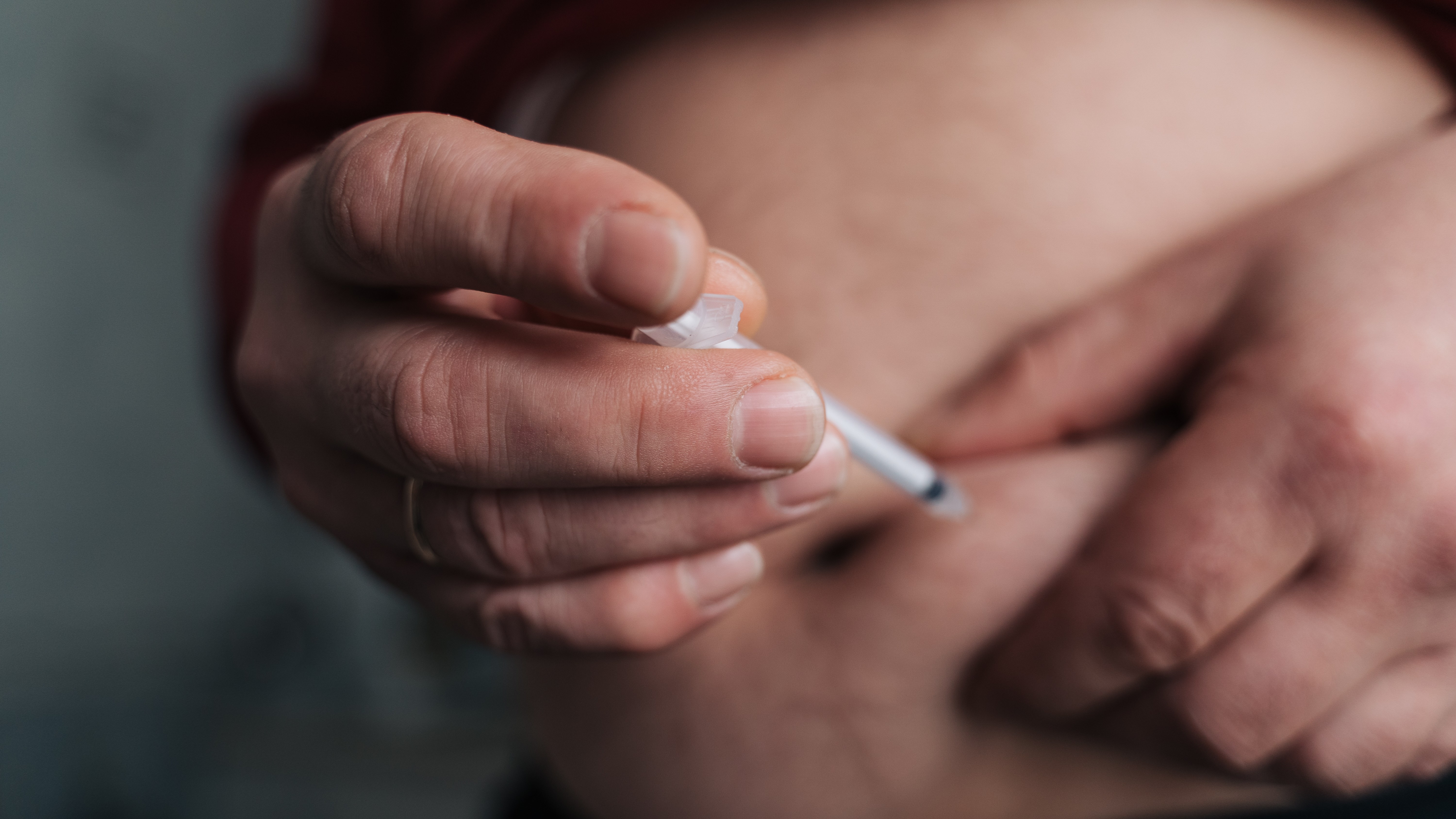 Close-up of a person's hand injecting insulin into their stomach.