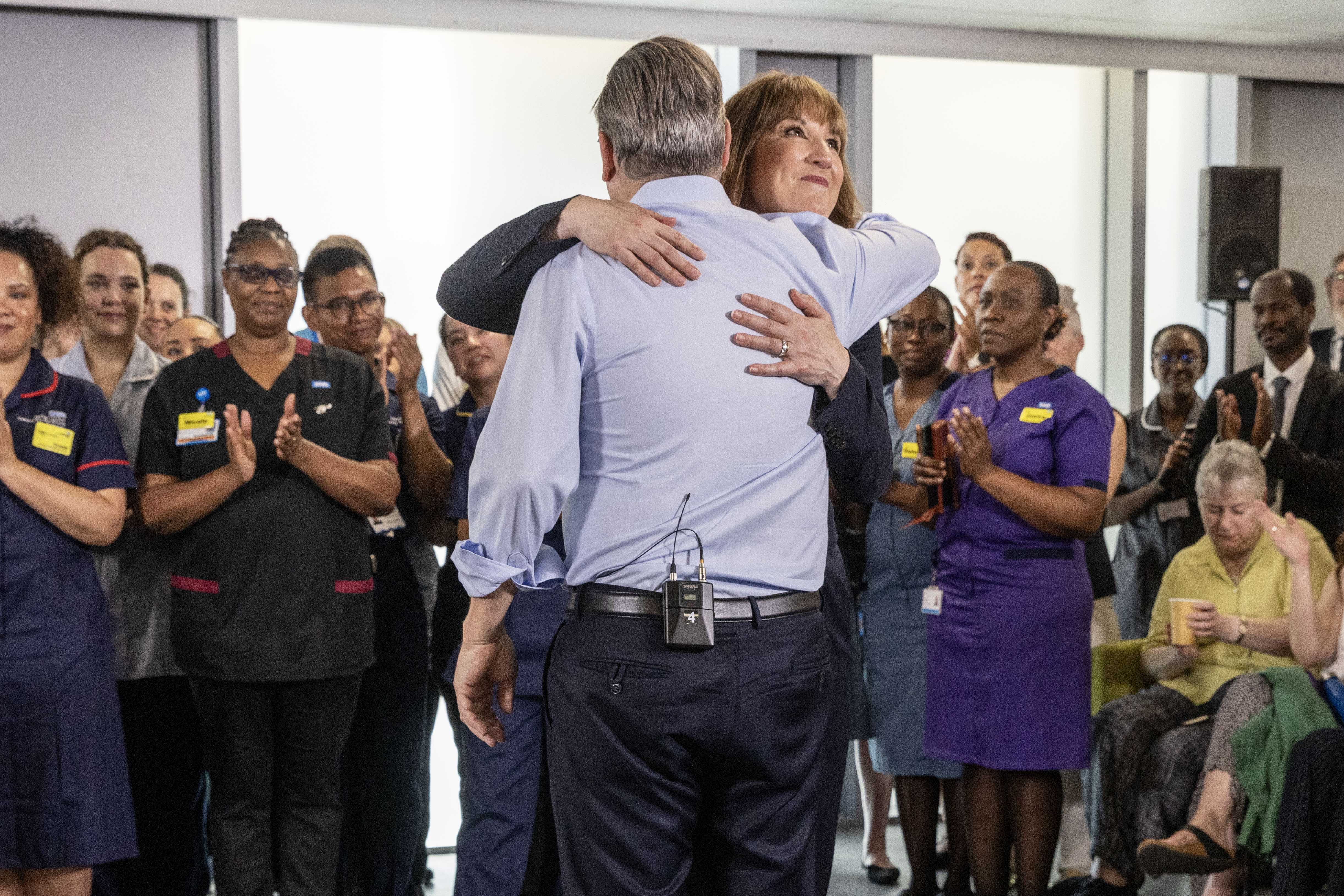 Rachel Reeves embracing Keir Starmer, surrounded by applauding NHS staff.