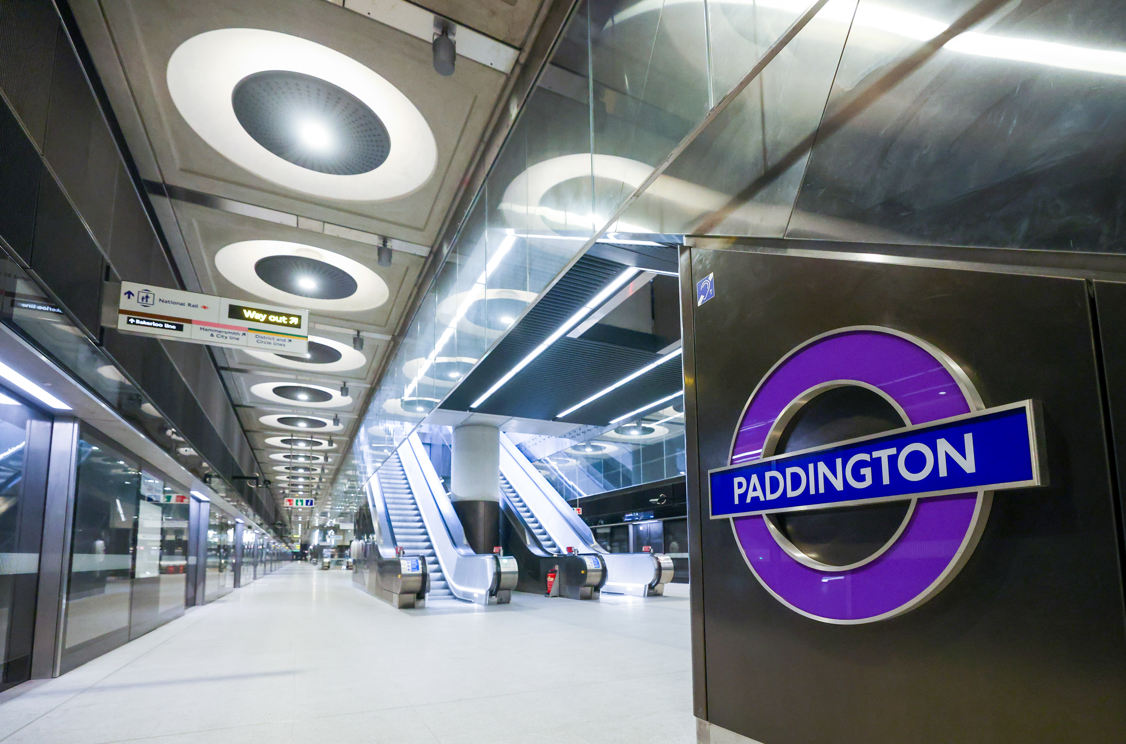 Paddington station platform on the Elizabeth Line in London, with escalators and a "Way Out" sign.