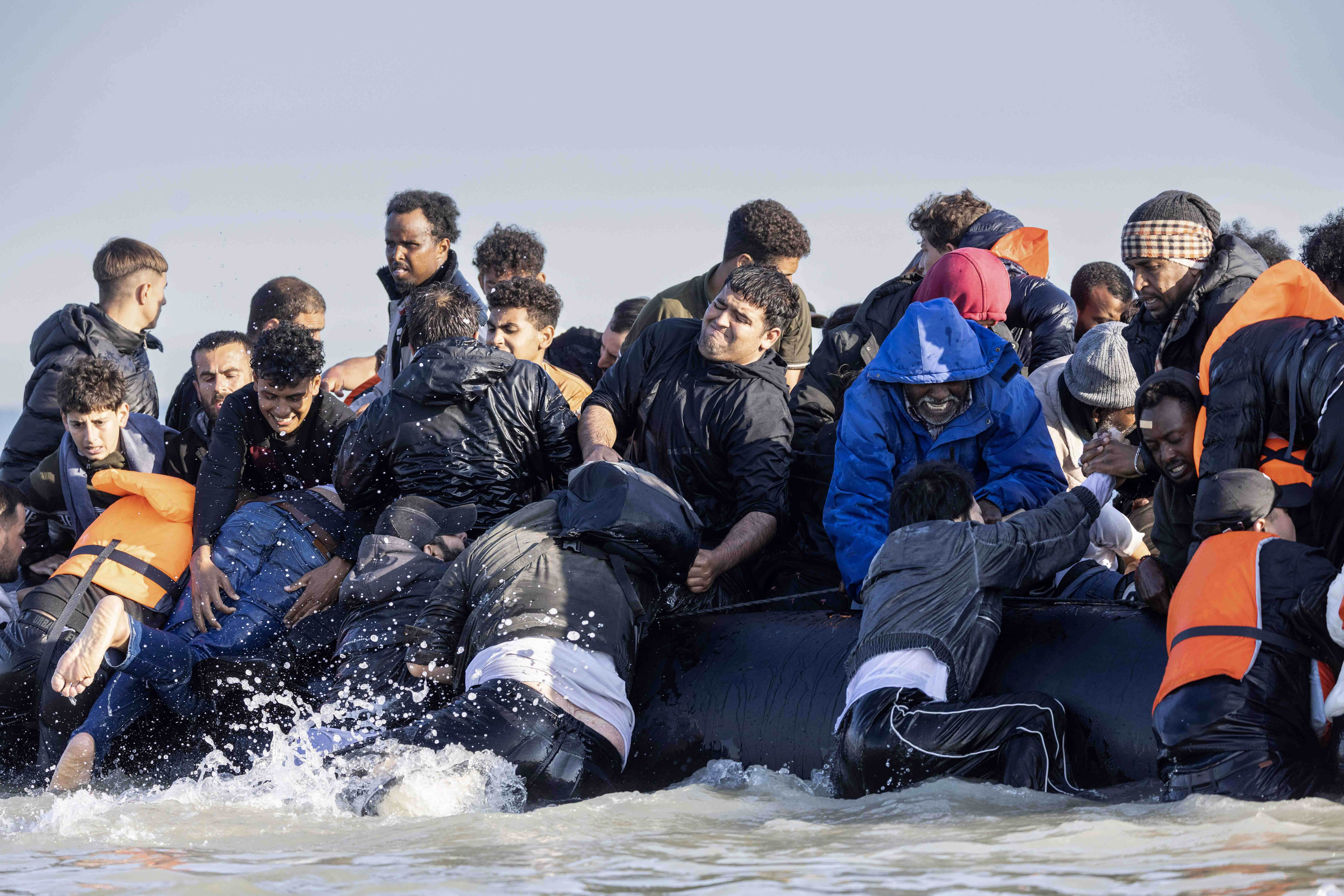 Migrants boarding a dinghy, splashing in the water.