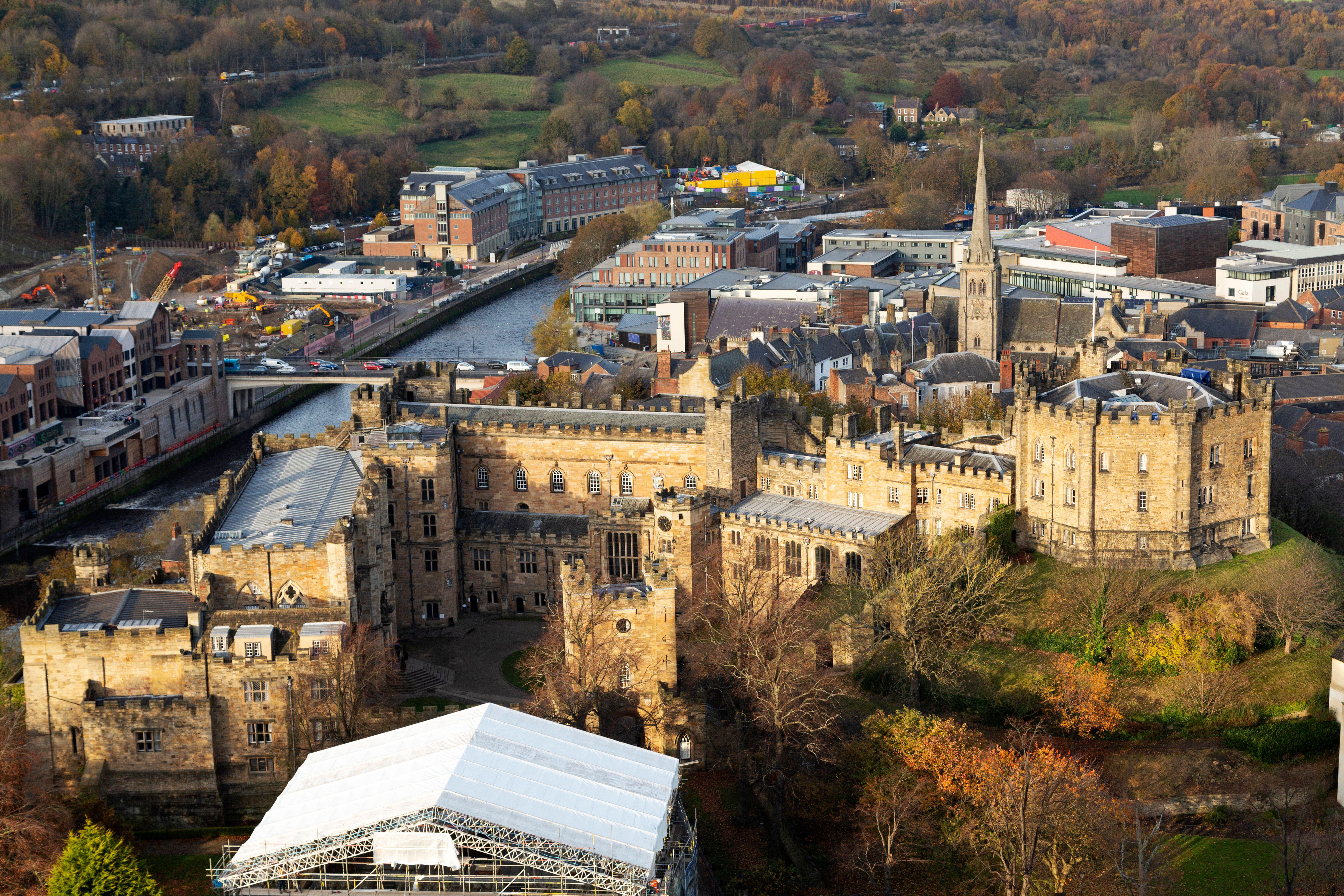 Aerial view of Durham Castle and surrounding city buildings, including a river and bridge, in autumn.