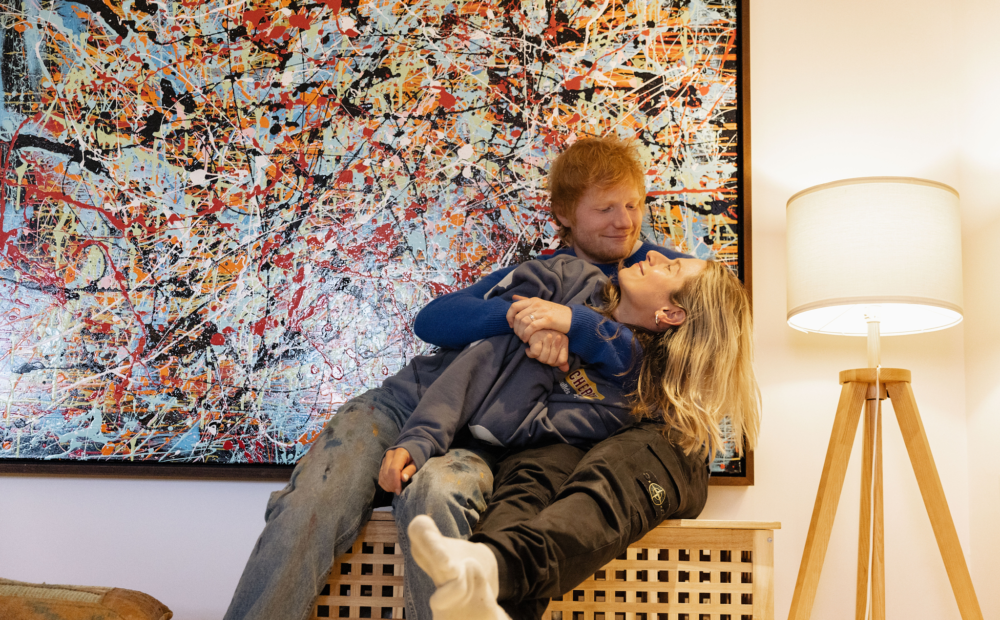 Ed Sheeran and Cherry Seaborn embracing each other, in front of a colorful abstract painting.
