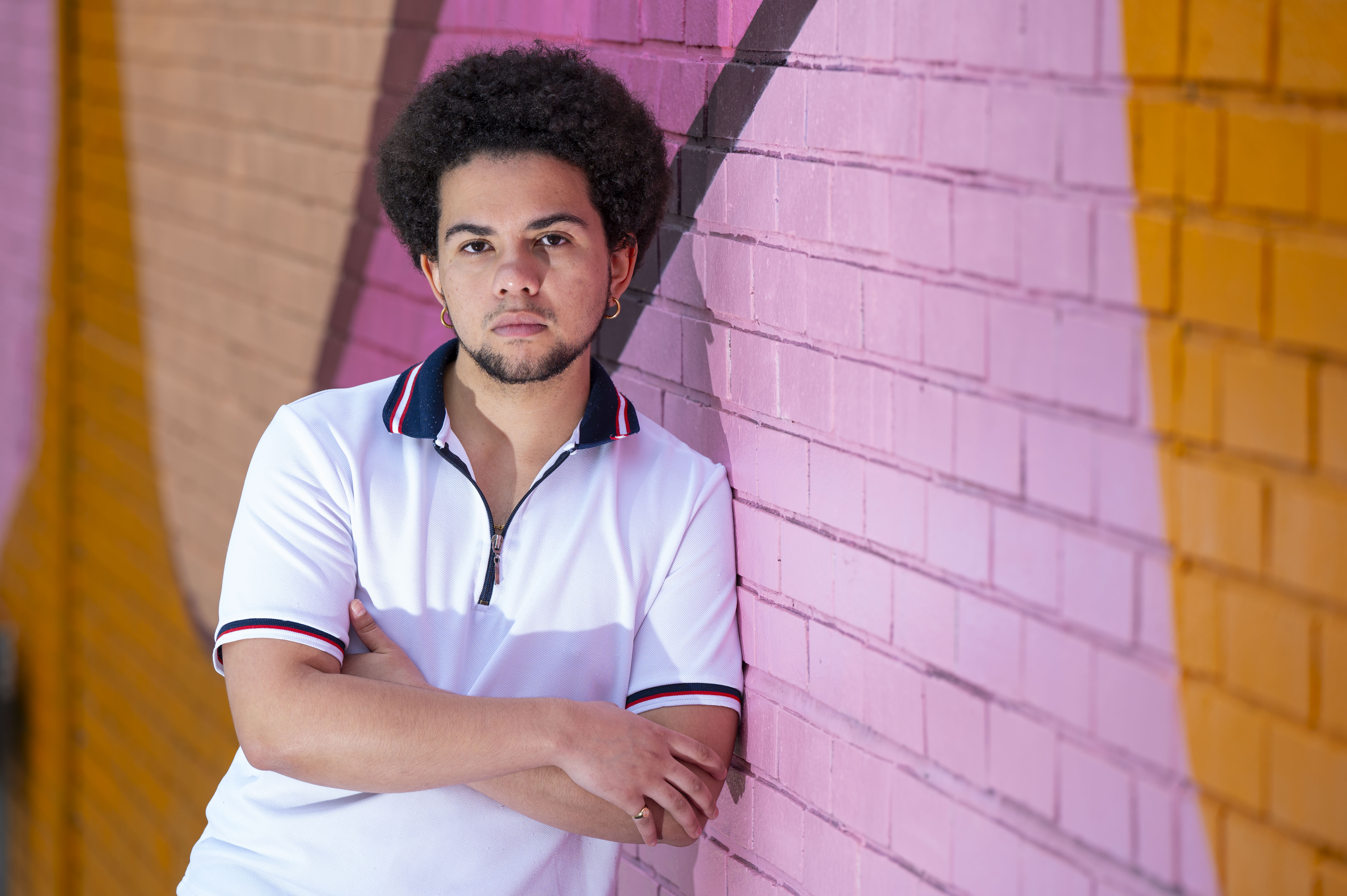 Keira Bell in a white polo shirt, leaning against a pink brick wall.