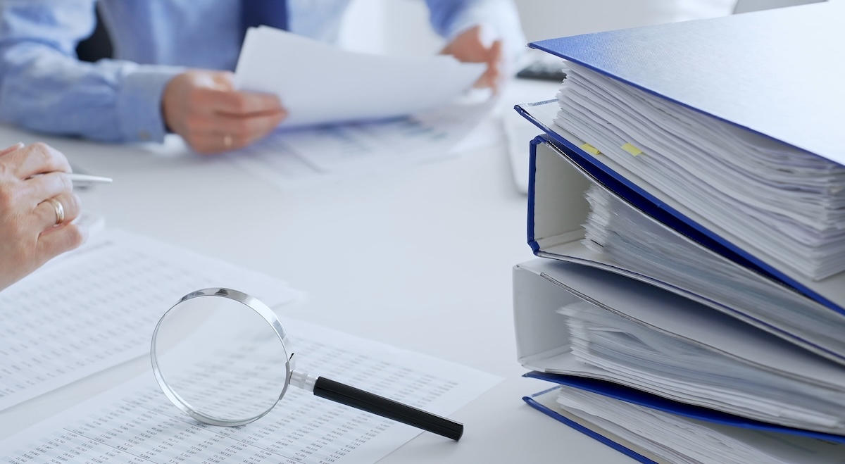 Accountants analyze financial reports in an office, flanked by a magnifying glass and documents.